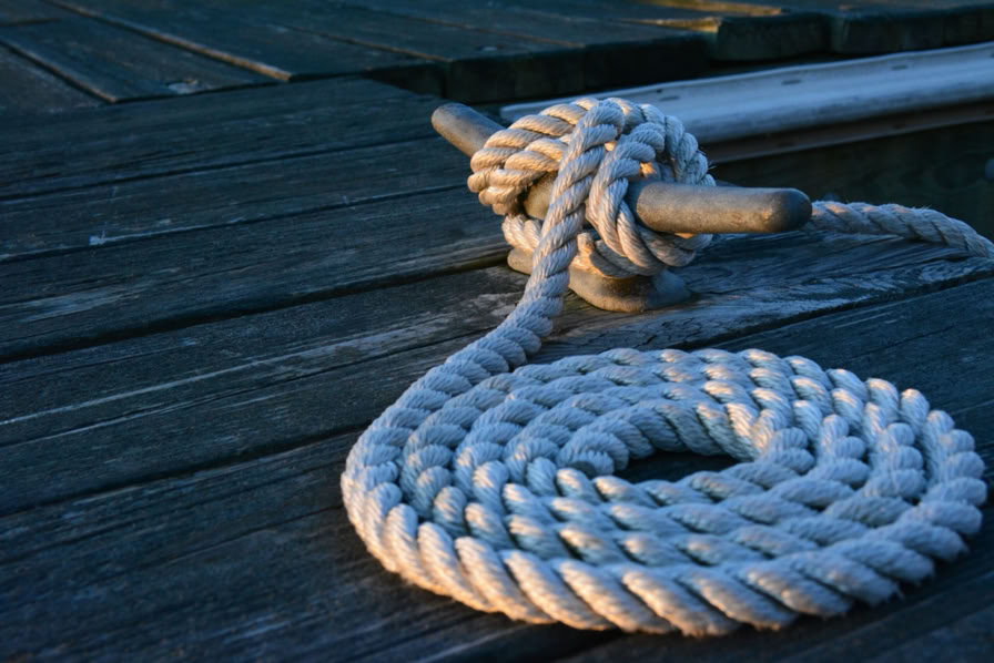 A coiled rope tied to a cleat on a wooden dock.