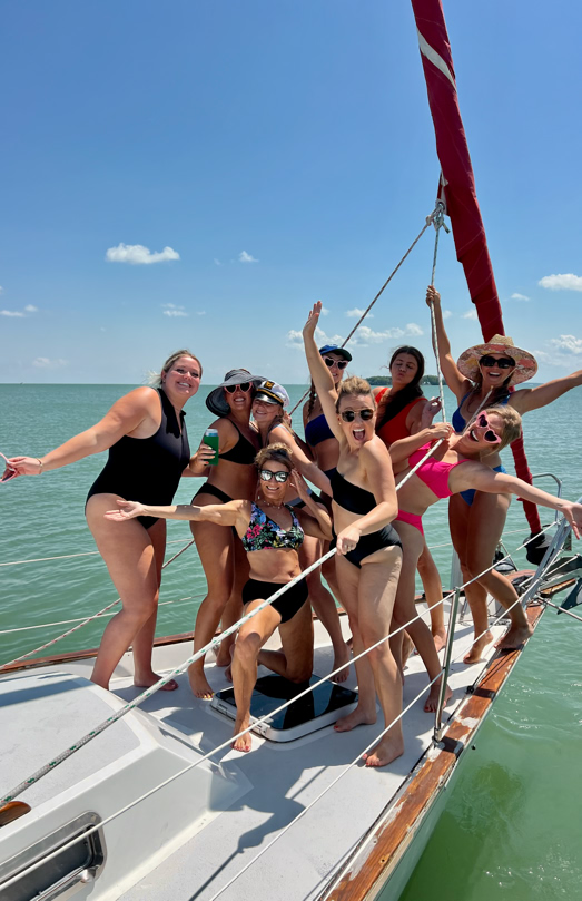 A group of people in swimwear posing on the deck of a sailboat on a sunny day.